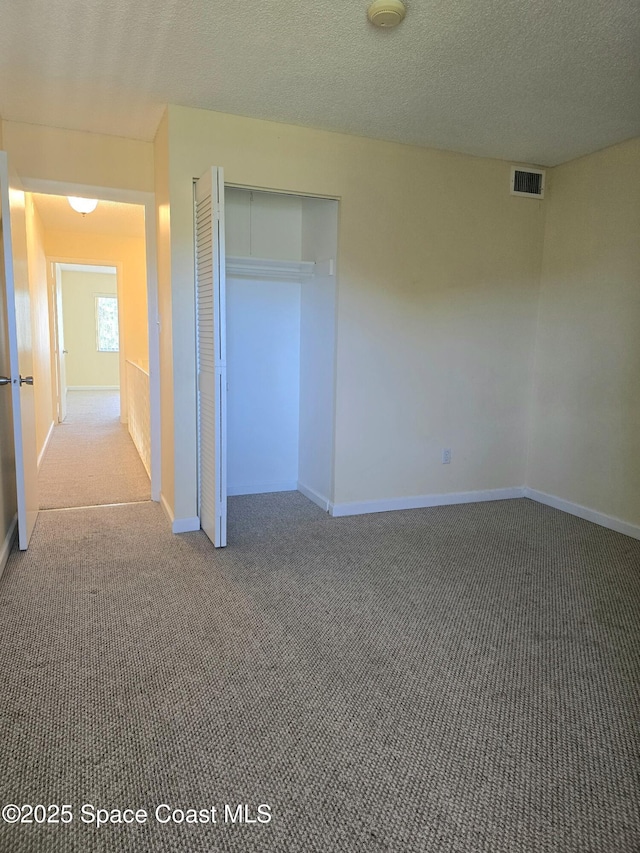 unfurnished bedroom featuring a textured ceiling, carpet flooring, visible vents, and baseboards