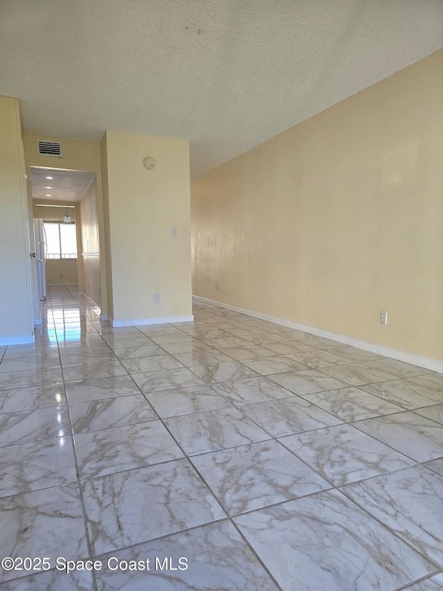 spare room with marble finish floor, baseboards, visible vents, and a textured ceiling