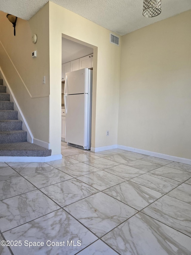 spare room featuring a textured ceiling, visible vents, baseboards, stairs, and marble finish floor