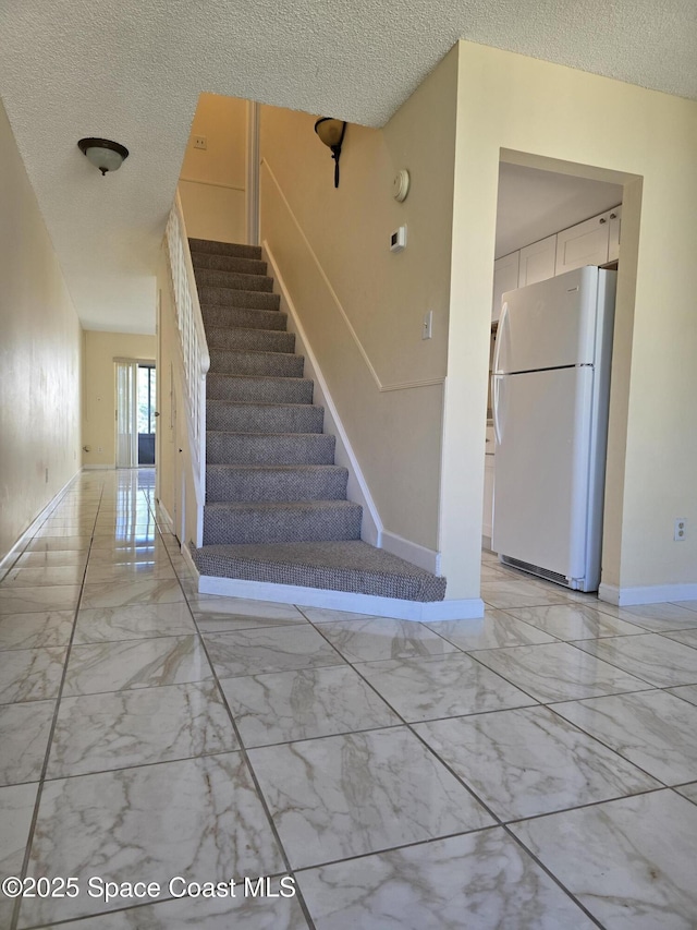 stairs with marble finish floor, baseboards, and a textured ceiling