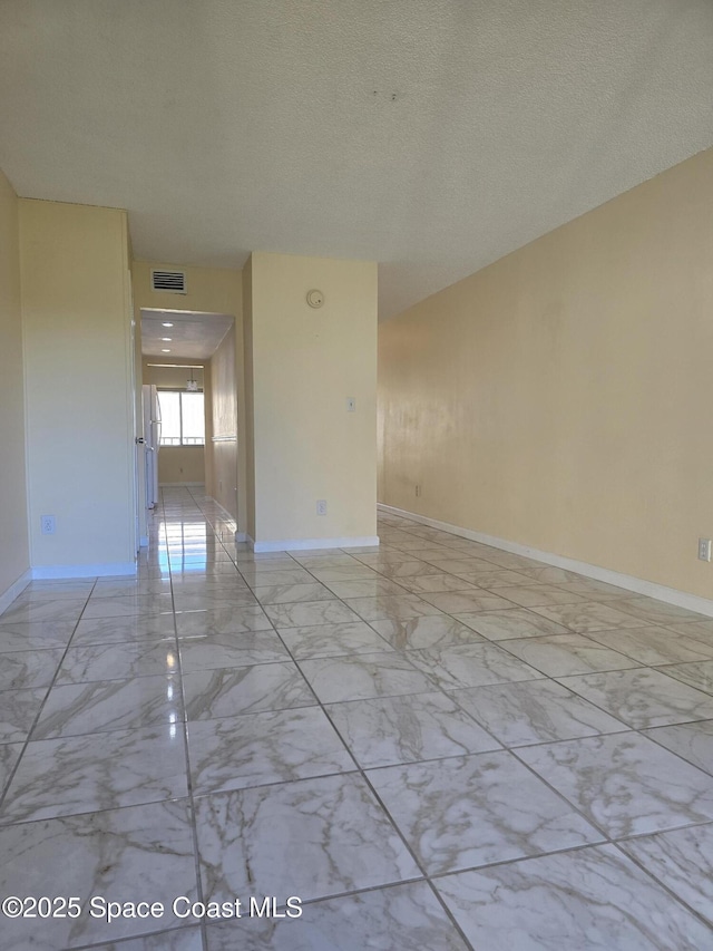 spare room with marble finish floor, visible vents, baseboards, and a textured ceiling