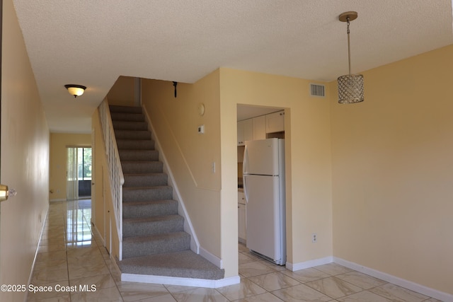 staircase featuring baseboards, visible vents, and a textured ceiling