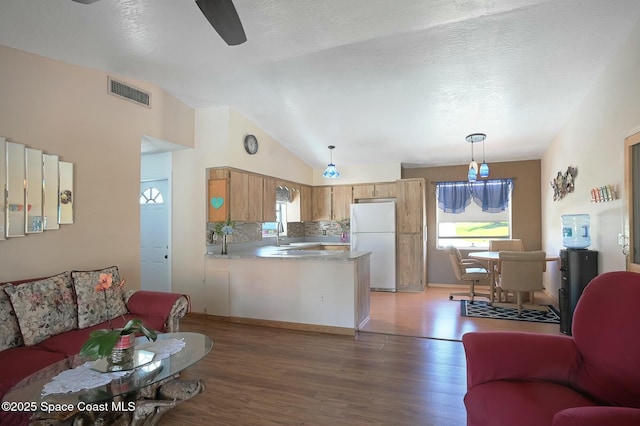 kitchen featuring visible vents, light wood-style floors, freestanding refrigerator, vaulted ceiling, and a peninsula