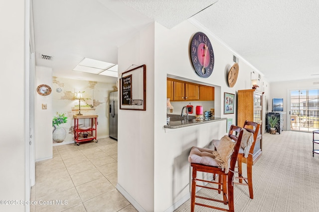 kitchen with visible vents, brown cabinets, stainless steel refrigerator with ice dispenser, light tile patterned flooring, and a textured ceiling