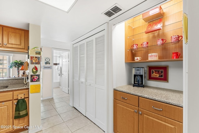 kitchen with light tile patterned flooring, visible vents, brown cabinets, and light stone counters