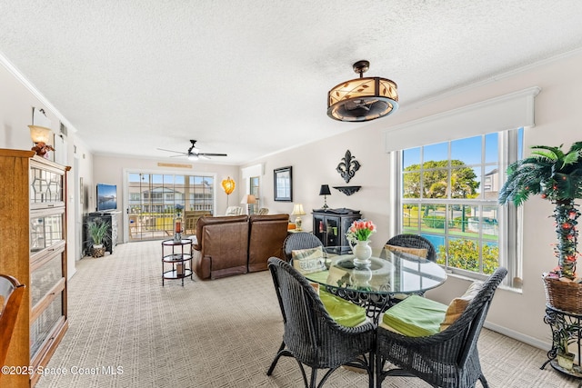 dining space with a ceiling fan, a textured ceiling, crown molding, baseboards, and light colored carpet