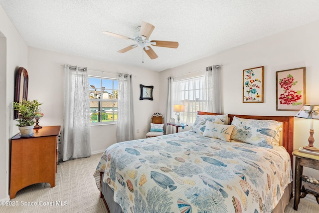 bedroom featuring a ceiling fan, multiple windows, light colored carpet, and a textured ceiling