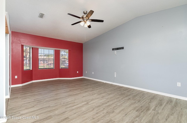 spare room featuring light wood finished floors, visible vents, baseboards, ceiling fan, and lofted ceiling