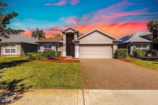 ranch-style house featuring stucco siding, driveway, an attached garage, and a yard