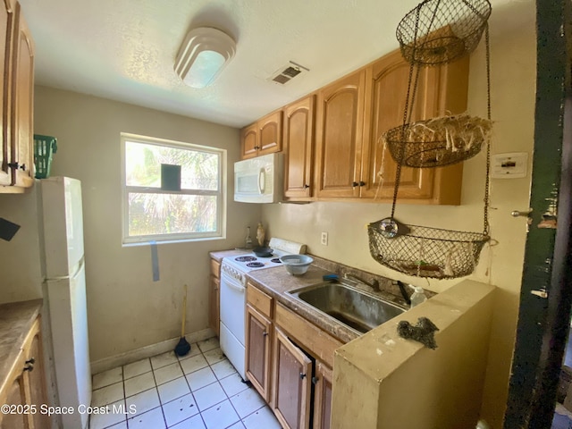 kitchen featuring light tile patterned floors, white appliances, a sink, visible vents, and baseboards