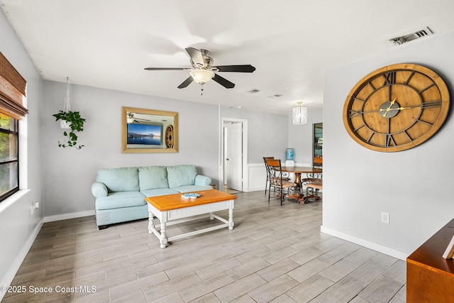 living area featuring baseboards, a ceiling fan, visible vents, and light wood-style floors