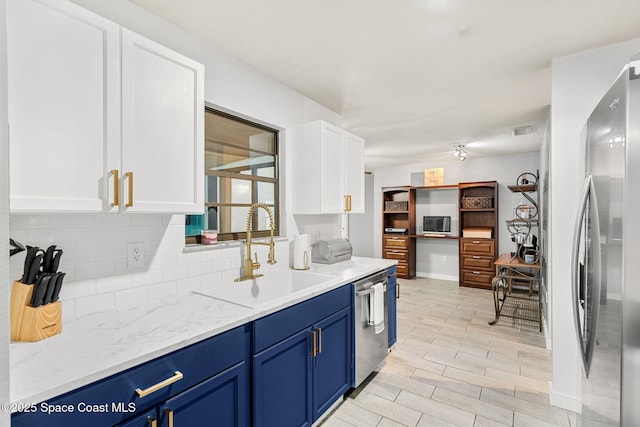 kitchen featuring a sink, white cabinets, blue cabinetry, appliances with stainless steel finishes, and decorative backsplash