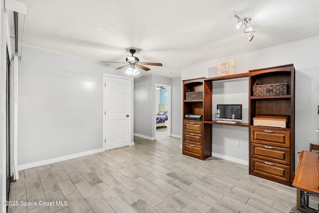 unfurnished office featuring a textured ceiling, a ceiling fan, baseboards, light wood-type flooring, and built in desk