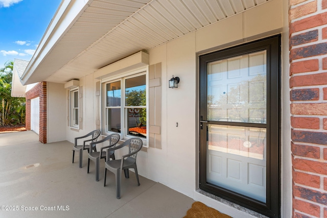 doorway to property with brick siding, a porch, and stucco siding