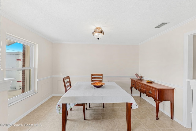 dining room featuring crown molding, a textured ceiling, visible vents, and wainscoting