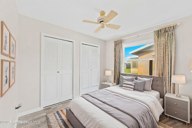 bedroom featuring two closets, baseboards, ceiling fan, and wood finished floors