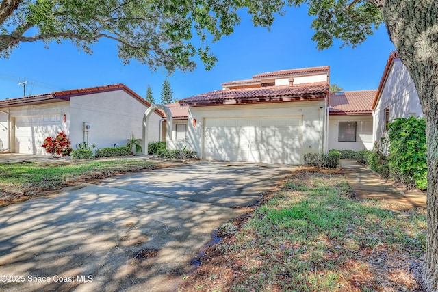 mediterranean / spanish-style house with a tile roof, an attached garage, driveway, and stucco siding