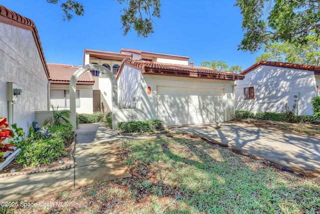 mediterranean / spanish-style home with a tile roof, stucco siding, concrete driveway, and a garage