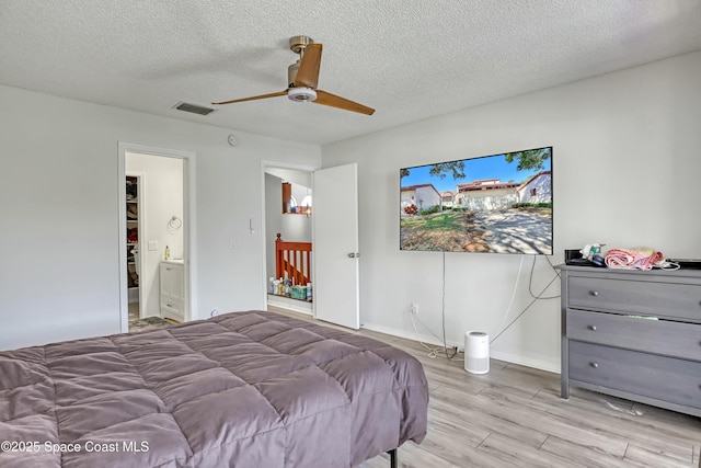 bedroom with light wood-type flooring, visible vents, a ceiling fan, a textured ceiling, and baseboards