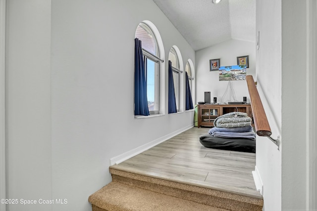 staircase featuring vaulted ceiling, wood finished floors, baseboards, and a textured ceiling