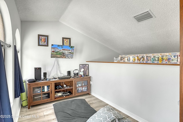 interior space with wood finished floors, baseboards, visible vents, vaulted ceiling, and a textured ceiling