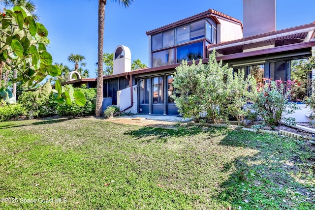 back of property featuring a lawn, a chimney, and a sunroom