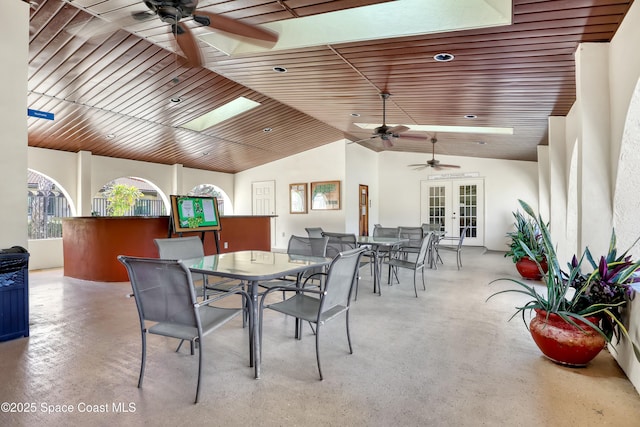 dining area with a ceiling fan, wood ceiling, french doors, concrete flooring, and vaulted ceiling