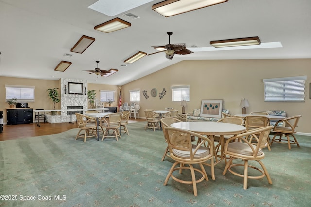 dining room with lofted ceiling with skylight, a ceiling fan, visible vents, and a large fireplace