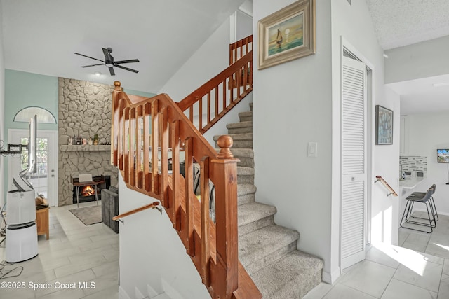 staircase with tile patterned floors, a textured ceiling, ceiling fan, and a fireplace