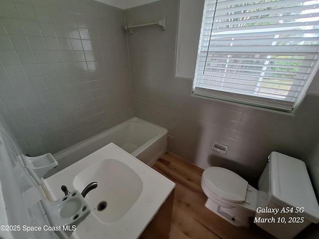 bathroom with toilet, bathing tub / shower combination, wood finished floors, tile walls, and a sink