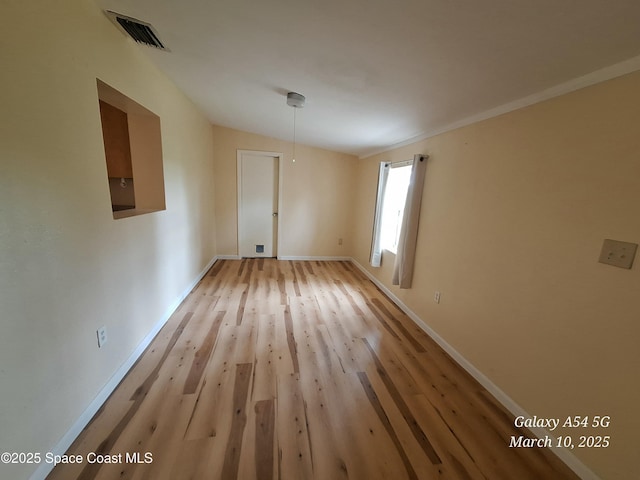 unfurnished room with vaulted ceiling, light wood-style flooring, baseboards, and visible vents