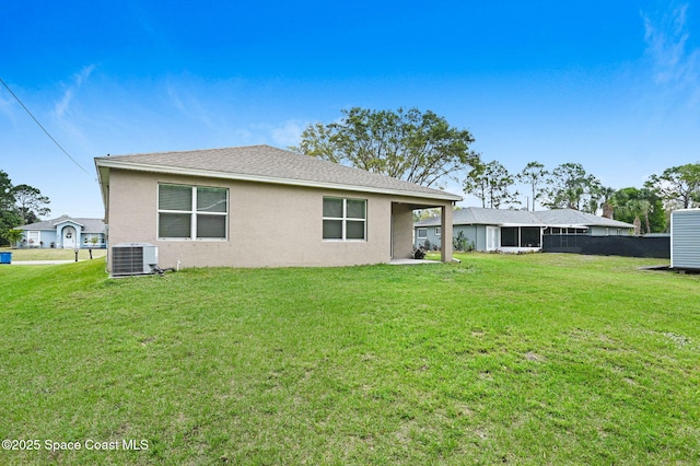 rear view of property featuring central air condition unit, a lawn, roof with shingles, and stucco siding