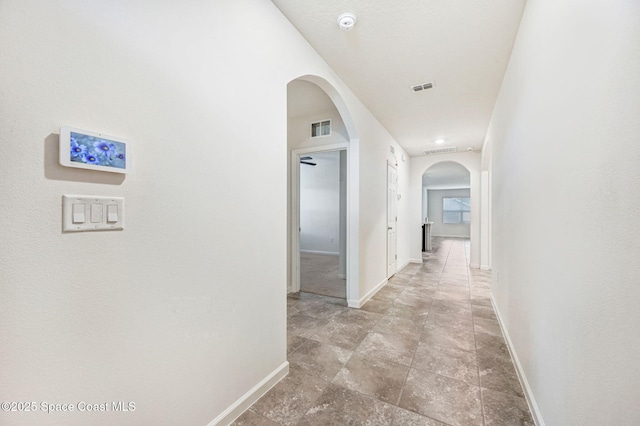 corridor featuring arched walkways, visible vents, and baseboards