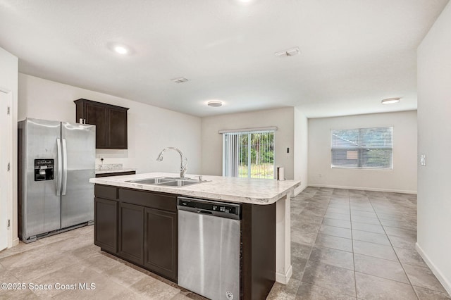 kitchen featuring a kitchen island with sink, a sink, stainless steel appliances, light countertops, and dark brown cabinetry