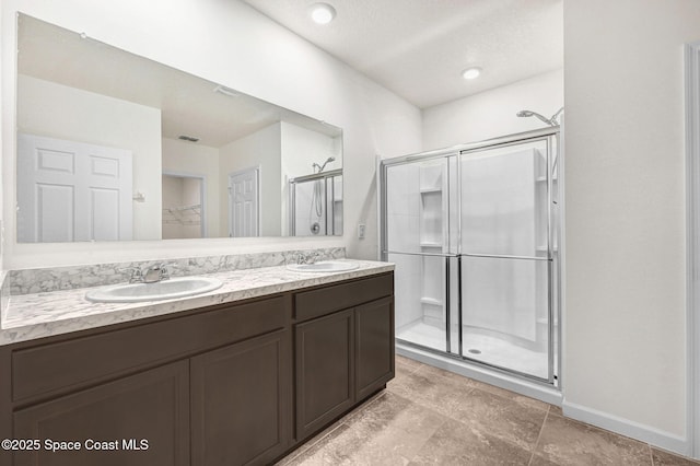 bathroom with double vanity, a shower stall, a walk in closet, and a sink