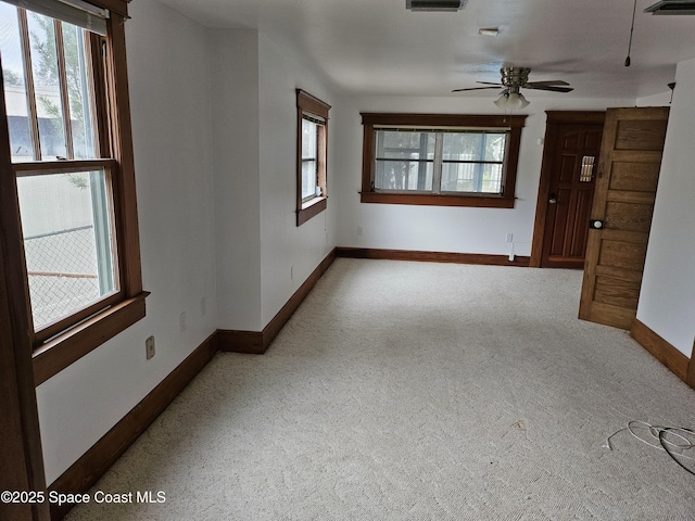 unfurnished living room with a ceiling fan, light colored carpet, a wealth of natural light, and baseboards