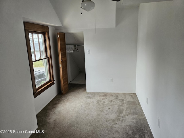 unfurnished bedroom featuring carpet floors, lofted ceiling, a walk in closet, and attic access