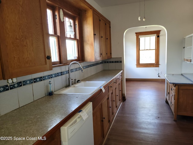 kitchen featuring dishwasher, tasteful backsplash, a sink, and brown cabinets