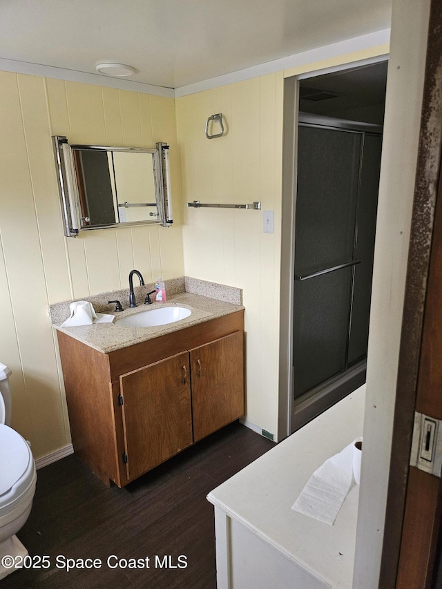 bathroom featuring toilet, vanity, wood finished floors, and a shower with shower door