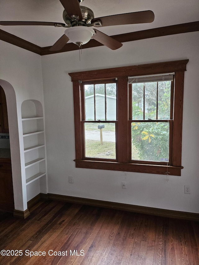 spare room featuring baseboards, built in shelves, arched walkways, and dark wood-type flooring