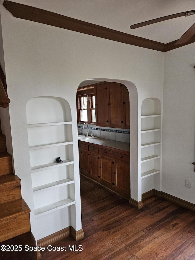 interior space featuring built in features, arched walkways, dark wood finished floors, a sink, and baseboards