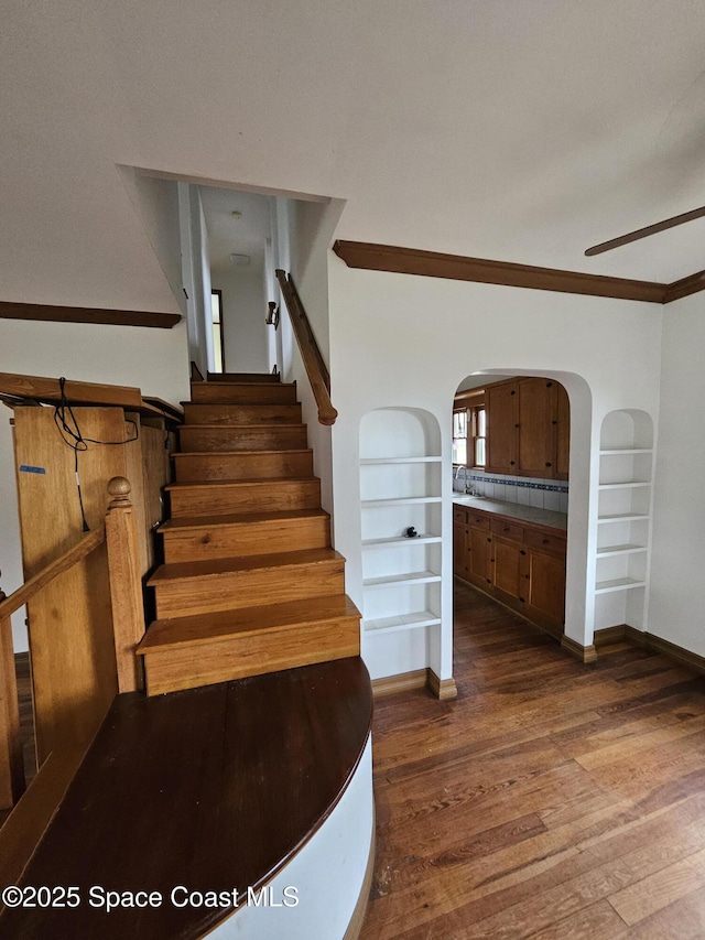 staircase featuring built in features, arched walkways, a ceiling fan, wood finished floors, and baseboards