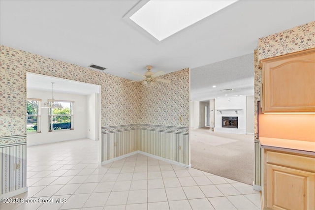 unfurnished room featuring visible vents, wallpapered walls, a fireplace with raised hearth, ceiling fan, and wainscoting