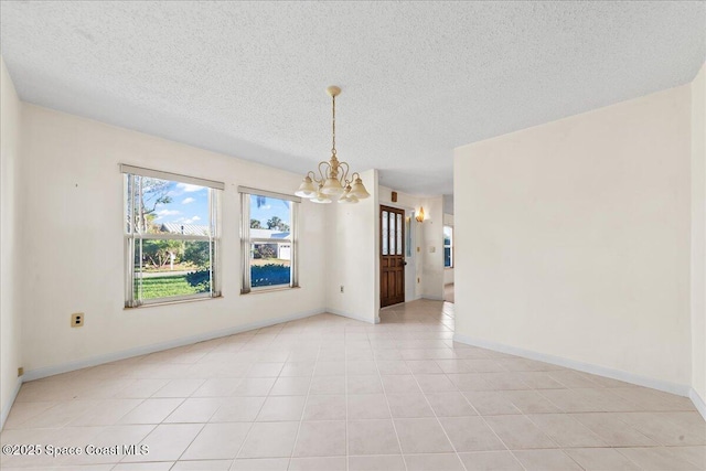 unfurnished room with light tile patterned floors, a notable chandelier, a textured ceiling, and baseboards