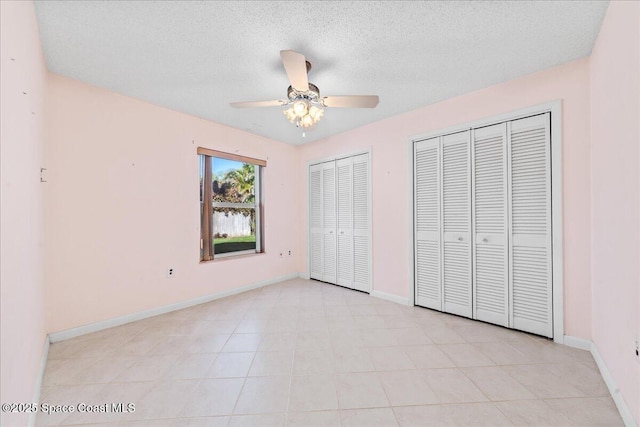 unfurnished bedroom with a ceiling fan, baseboards, two closets, and a textured ceiling