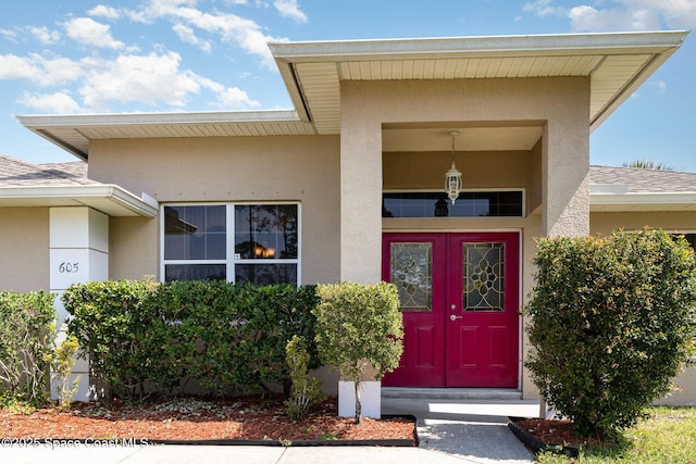 view of exterior entry with stucco siding and roof with shingles