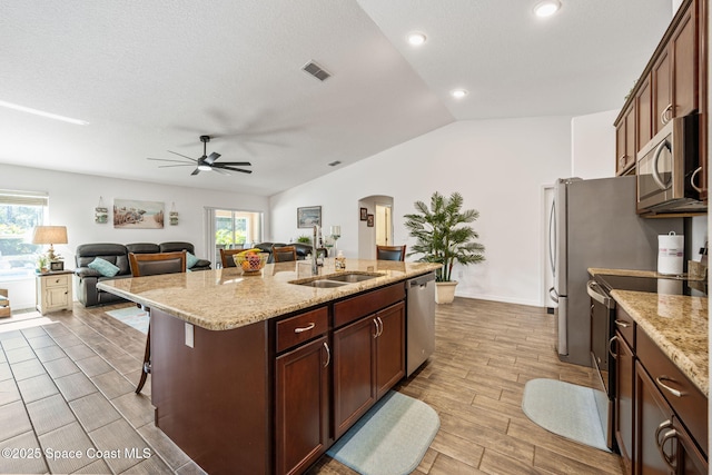 kitchen with visible vents, a center island with sink, a sink, stainless steel appliances, and vaulted ceiling