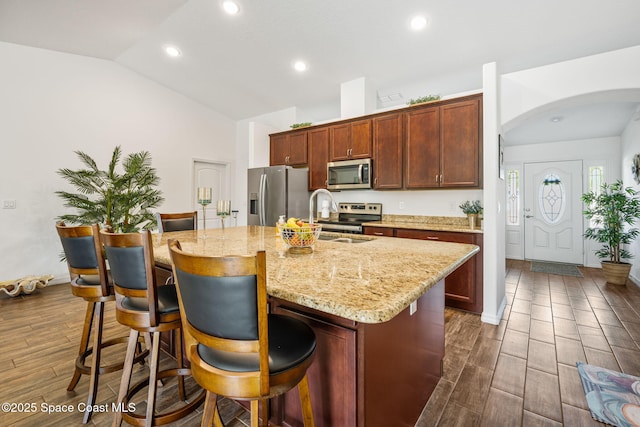 kitchen featuring lofted ceiling, a center island with sink, appliances with stainless steel finishes, and wood finish floors