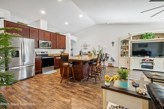 kitchen featuring dark wood finished floors, open floor plan, a breakfast bar area, lofted ceiling, and stainless steel appliances