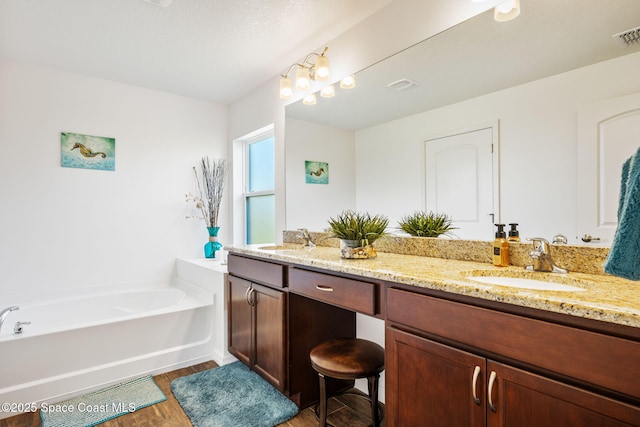 full bathroom with double vanity, a garden tub, wood finished floors, and a sink